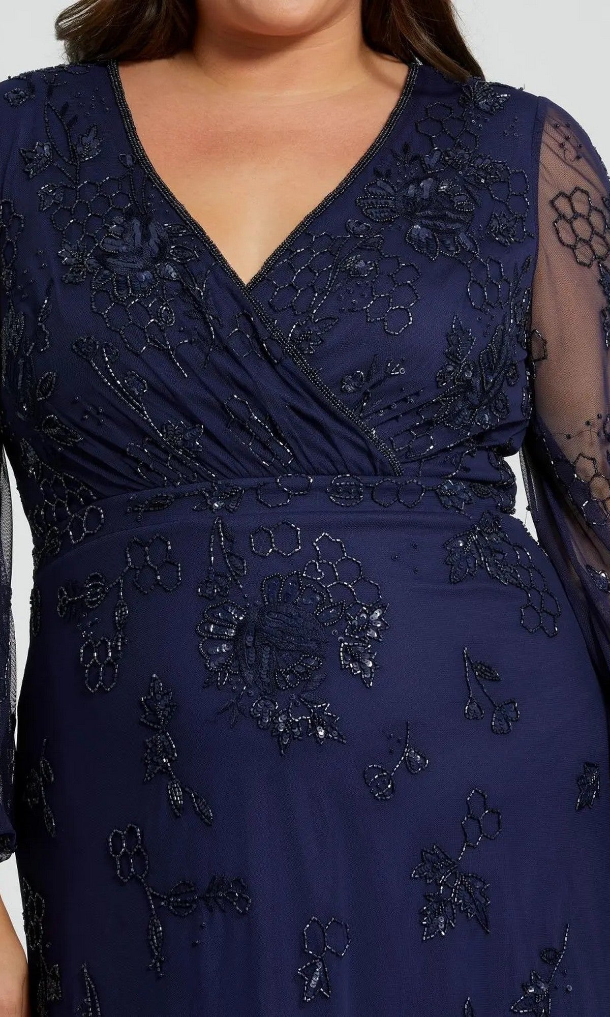 Close-up of a person wearing the Mac Duggal 9247 long plus-size formal dress in navy, featuring floral embroidery, a V-neckline, and elegant dark blue long sleeves for a sophisticated look.