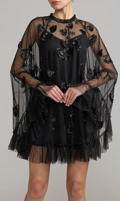 A person wearing the Mac Duggal 9257 Long Sleeve Short Hoco Dress, featuring sheer long sleeves, ruffled layers, and black appliqué embellishments in floral and fan shapes—an elegant look that showcases Mac Duggal’s signature style.
