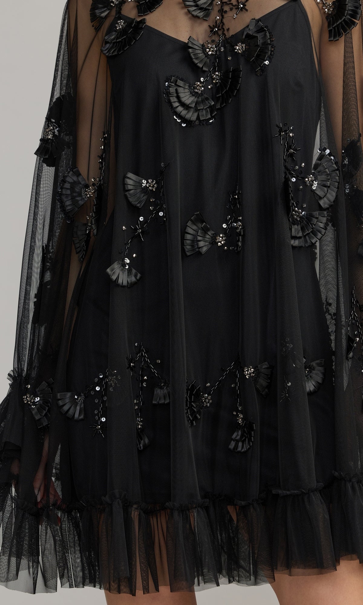 A close-up of the Mac Duggal 9257 Long Sleeve Short Hoco Dress, showcasing black mesh fabric with elegant 3D floral appliqués, sequin embellishments, and ruffled hem details that evoke the style of a chic homecoming party dress.