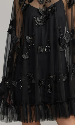 A close-up of the Mac Duggal 9257 Long Sleeve Short Hoco Dress, showcasing black mesh fabric with elegant 3D floral appliqués, sequin embellishments, and ruffled hem details that evoke the style of a chic homecoming party dress.