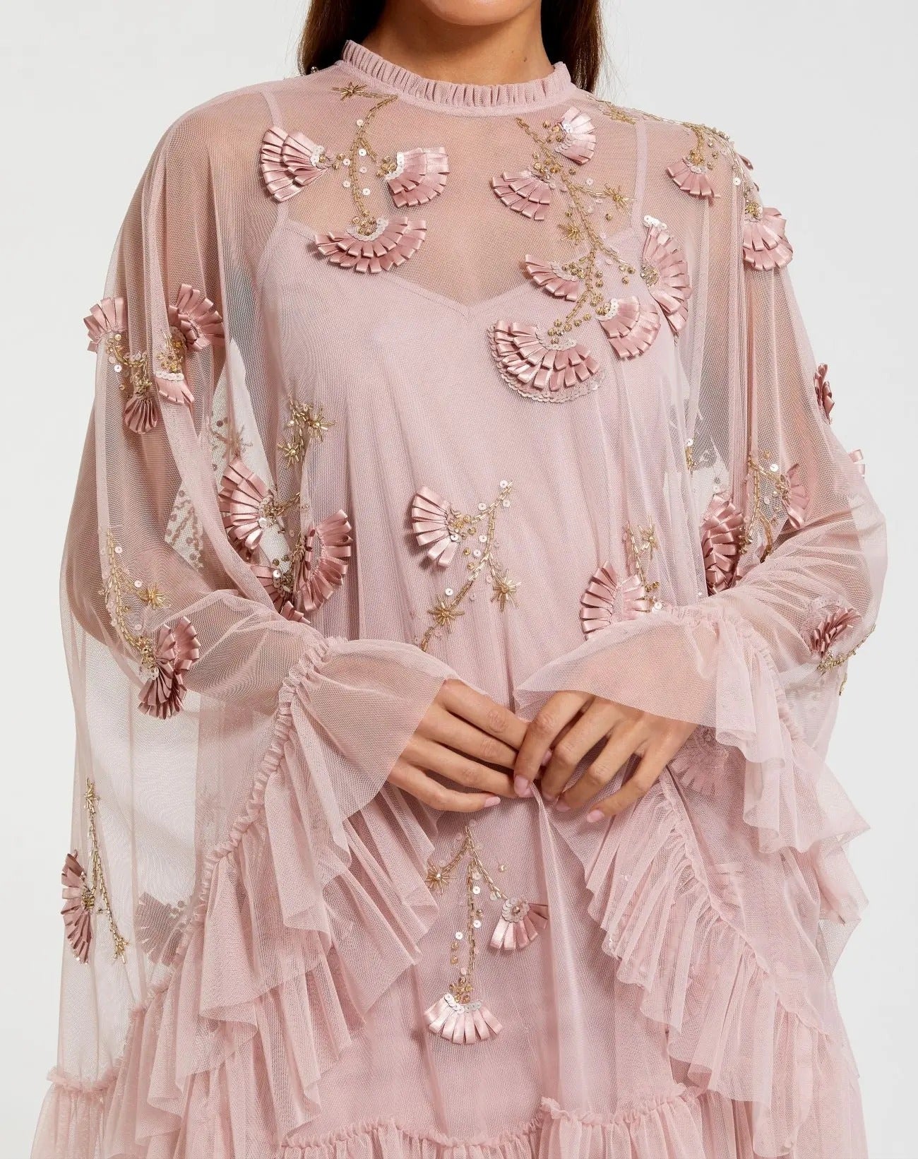 A person wearing the Mac Duggal 9257 Long Sleeve Short Hoco Dress in light pink, featuring sheer ruffles and floral appliqué, with hands folded at the waist.