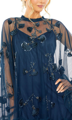 Woman in a Mac Duggal 9257 Long Sleeve Short Hoco Dress, navy blue with sheer fabric and floral leaf appliqués, poses stylishly with one hand on her hip.