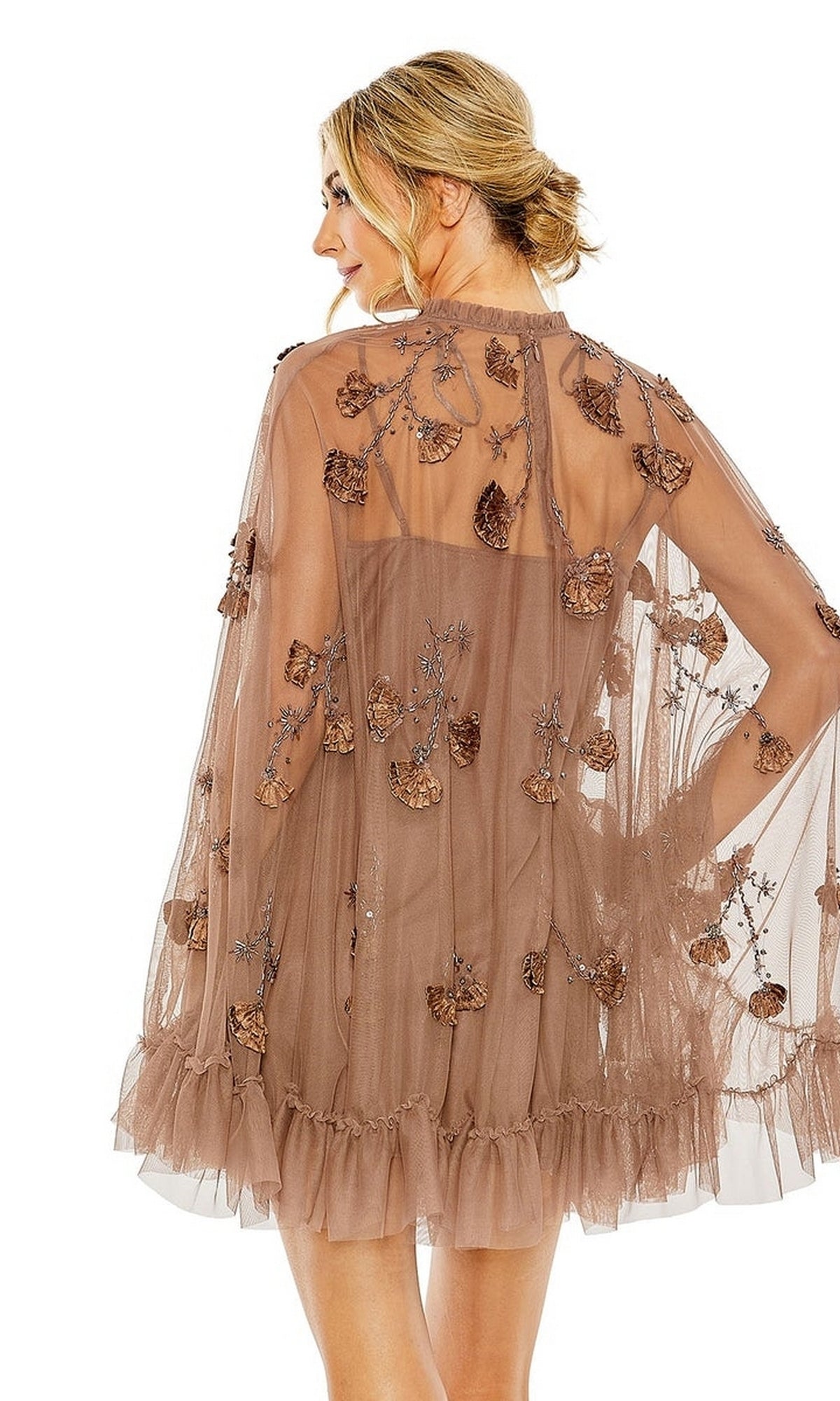 A woman models the Mac Duggal 9257 Long Sleeve Short Hoco Dress, a sheer light brown party dress with leaf embroidery and a ruffled hem, posing with her back to a white background.