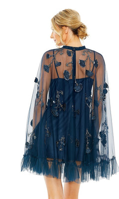 A woman is seen from the back wearing the Mac Duggal 9257 Long Sleeve Short Hoco Dress in dark blue with sheer fabric, floral embroidery, and tulle details, set against a white background.