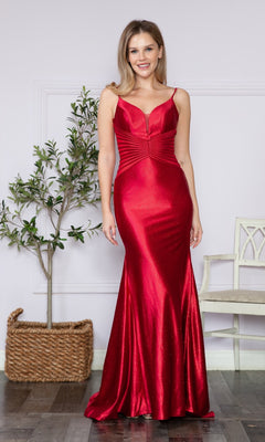 A woman smiles at the camera indoors, standing near a potted plant and white chair, wearing the Sheer Cut-Out Sides Long Prom Dress 9260—a shiny red v-neck evening gown.