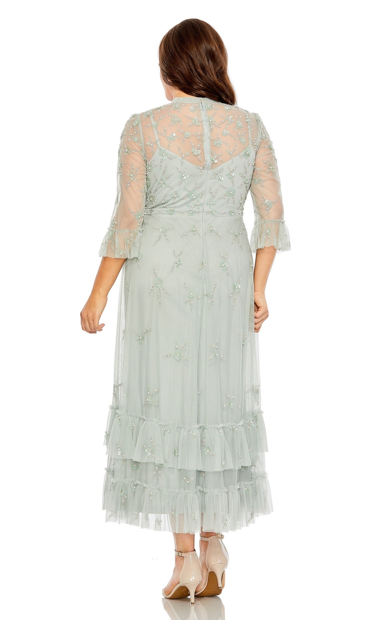 A woman with long brown hair and beige heels faces away, modeling the Tea-Length Plus-Size Formal Dress 9263 by Mac Duggal—a light blue A-line dress featuring sheer sleeves, floral embroidery, and a ruffled hem.