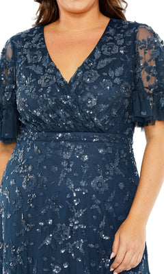 A person wearing the Long Plus-Size Formal Dress 9270 by Mac Duggal, featuring dark blue sequins, an A-line silhouette, short sheer sleeves, and a V-neckline.