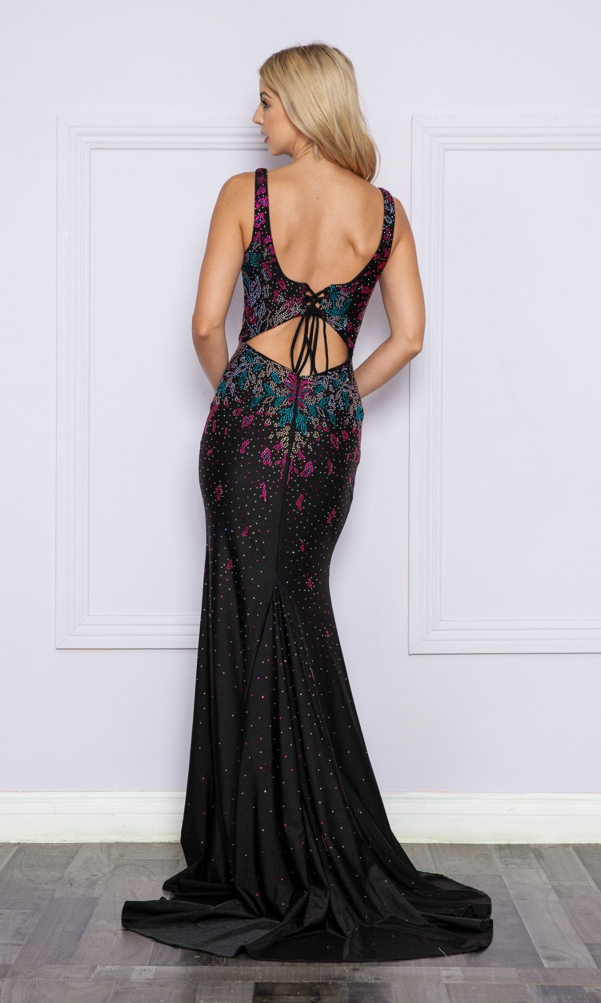 A woman stands facing away in the Multi-Color Beaded Long Black Formal Dress 9270, featuring an open back, lace-up detail, and vibrant beaded accents—a bold modern take on classic formalwear.