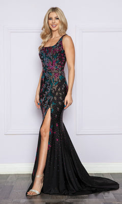 A woman stands indoors wearing the Multi-Color Beaded Long Black Formal Dress 9270, which features a sleeveless design, floor length, colorful sequin patterns, a thigh-high slit, and clear high-heeled sandals.
