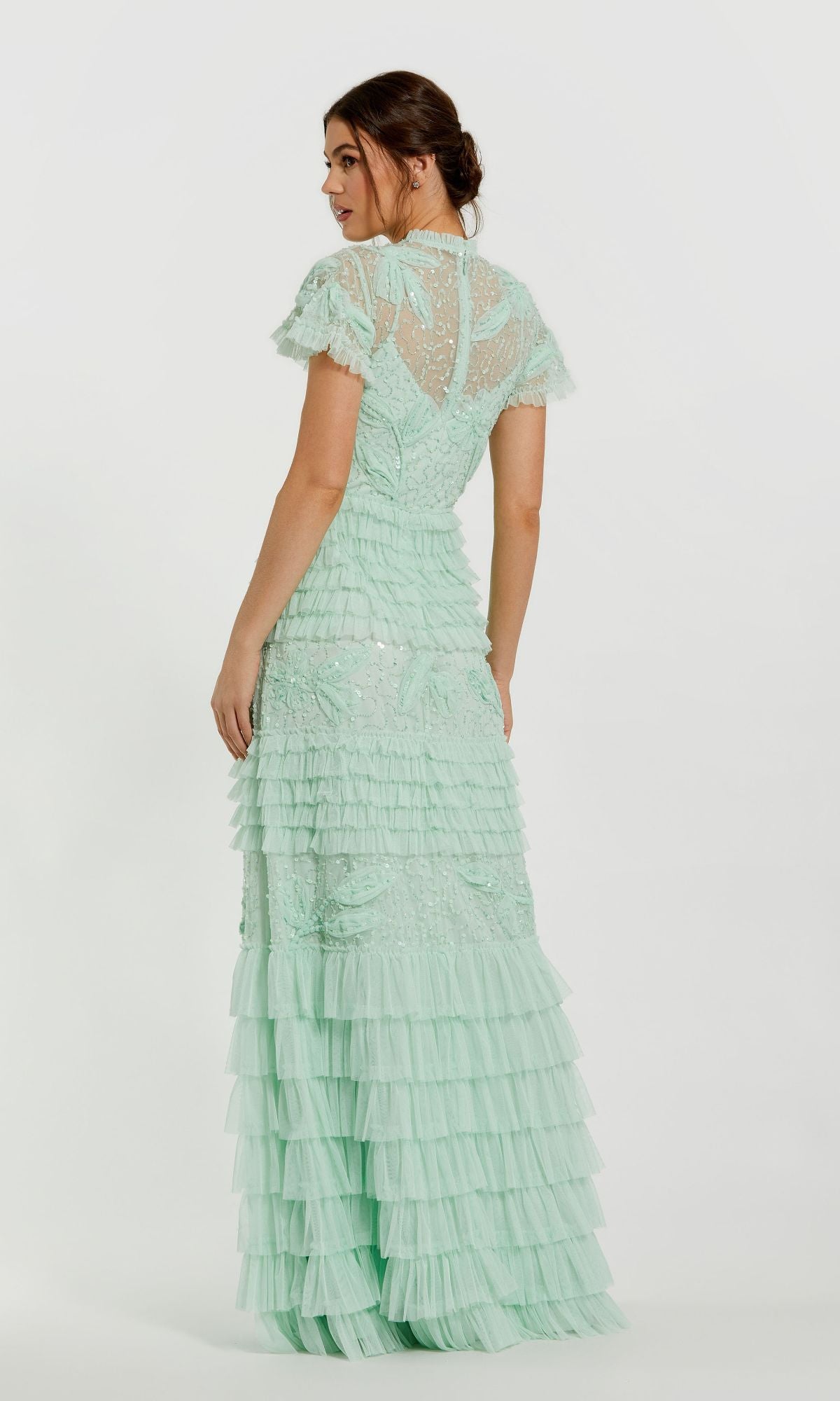 A woman in a long sage green formal dress, Mac Duggal 9278, with ruffled lace and short sleeves stands slightly turned from the camera, showcasing the gown's elegant design.