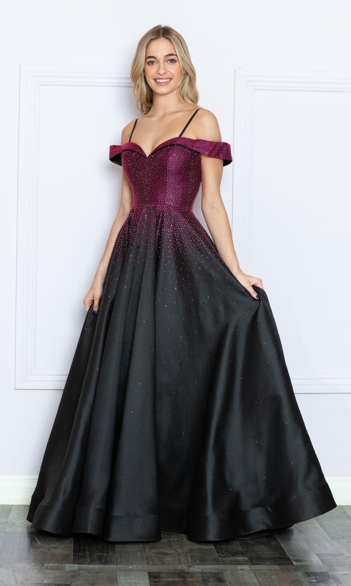 A woman stands in a formal setting, wearing the Cold-Shoulder Beaded Long Prom Ball Gown 9278 featuring an off-the-shoulder sparkling magenta bodice and a full black skirt with magenta accents.