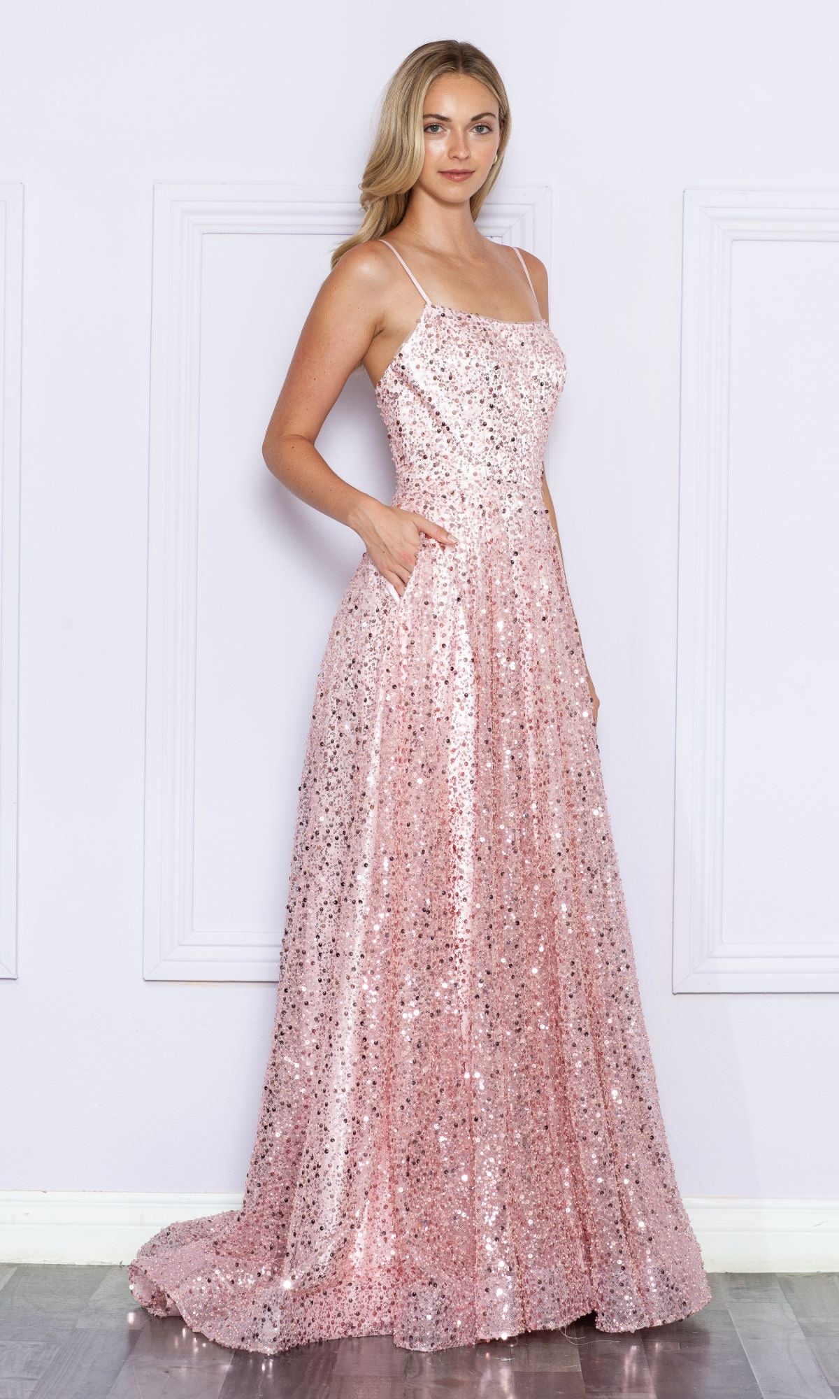 A woman in the Long Sequin A-Line Prom Dress with Pockets 9290 stands against a white wall with decorative paneling.