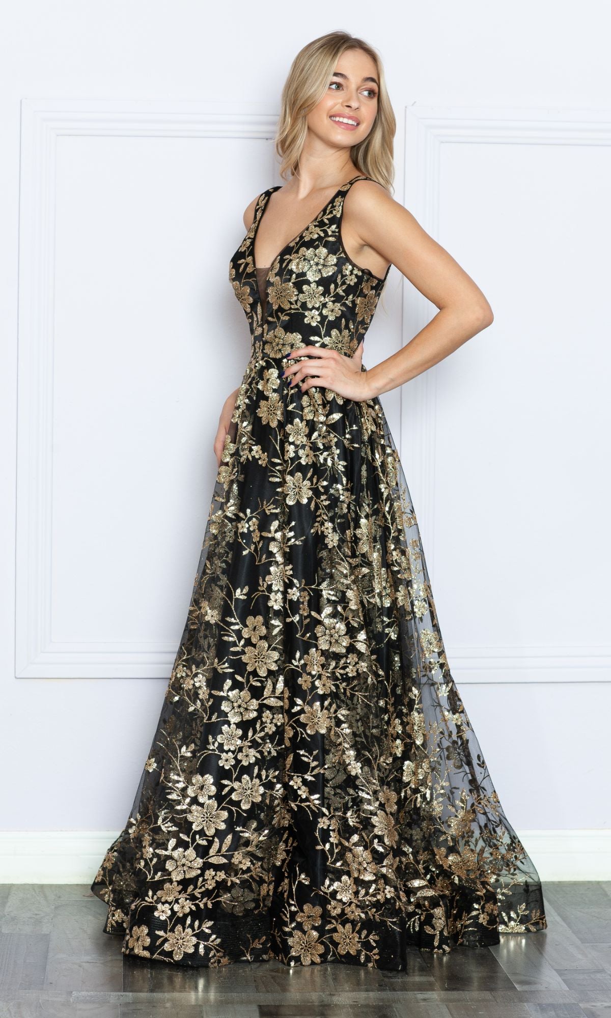 Woman in the Glitter-Floral-Print Long A-Line Prom Dress 9298, featuring a sleeveless V-neck and gold floral embroidery, stands sideways and smiles against a white background.