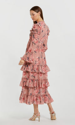 A woman stands sideways against a plain white background wearing the Mac Duggal 9306 Midi Wedding Guest Dress, a long-sleeved, tiered pink floral chiffon dress with ruffles.