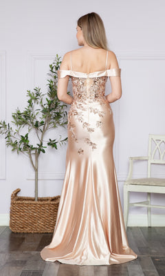 A woman faces away from the camera indoors in the Embellished Off-the-Shoulder Long Prom Dress 9350, a champagne-colored gown with floral embroidery, shimmering near a potted plant and white chair.