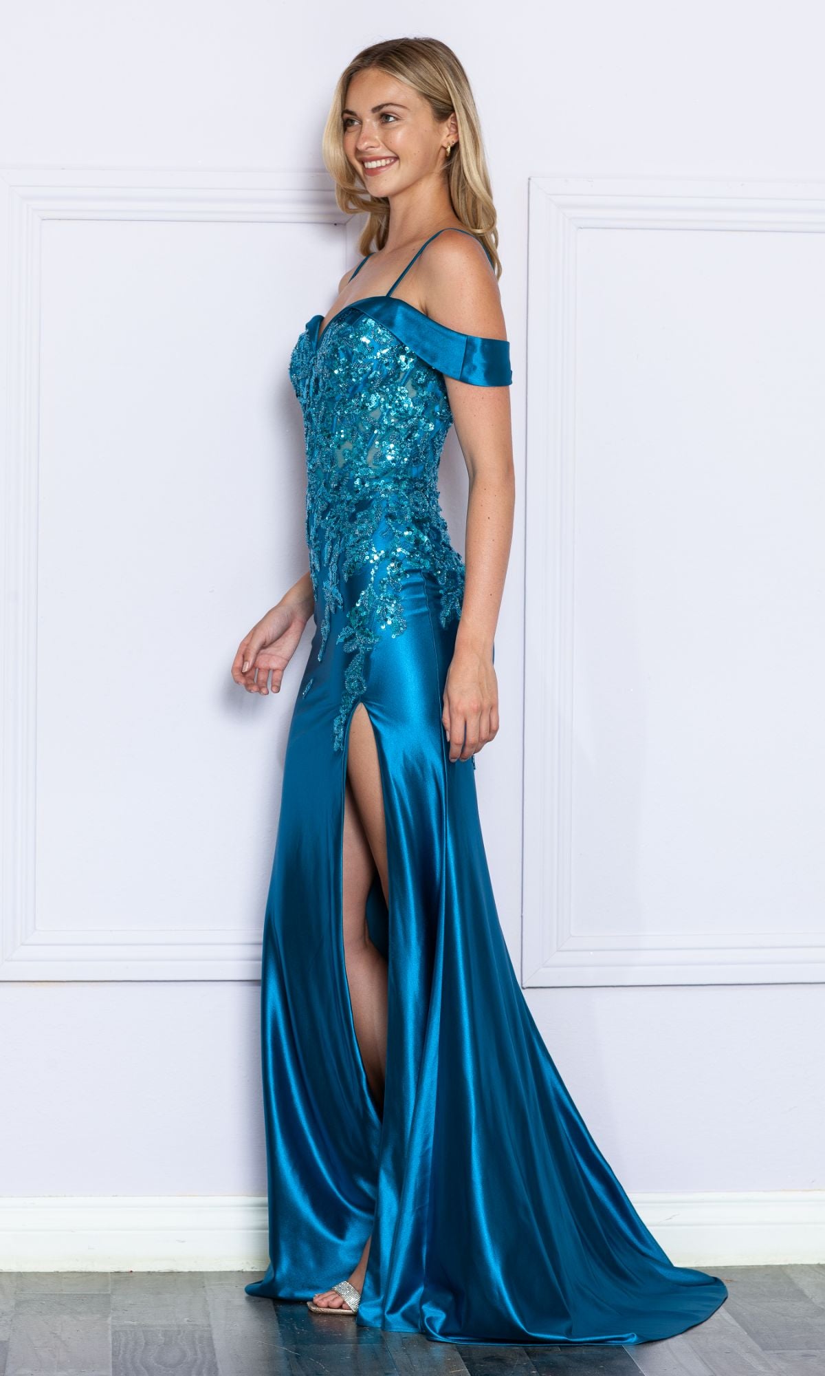 A woman poses against a light wall in the Embellished Off-the-Shoulder Long Prom Dress 9350—a fitted teal satin gown with sequins and a high leg slit—ideal as a formal dress for proms or special occasions.