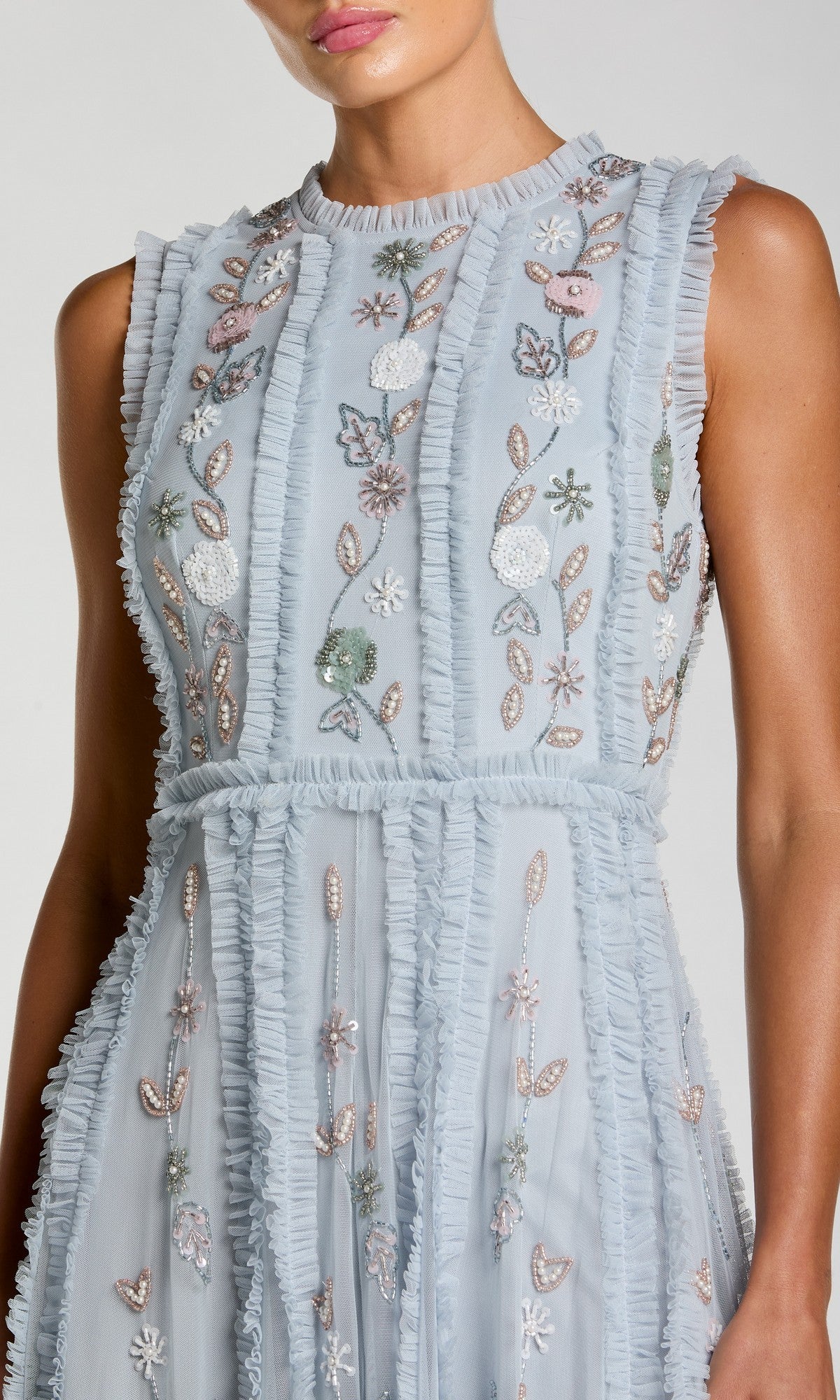 A woman wearing the Mac Duggal 9360, a sleeveless long sage formal dress with ruffled edges and pastel floral embroidery.