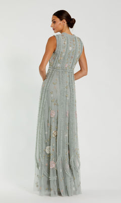 A woman stands with her back to the camera in a Mac Duggal 9360 Sleeveless Long Sage Formal Dress, a floor-length pastel gown with delicate floral embroidery and beading, set against a plain white background.