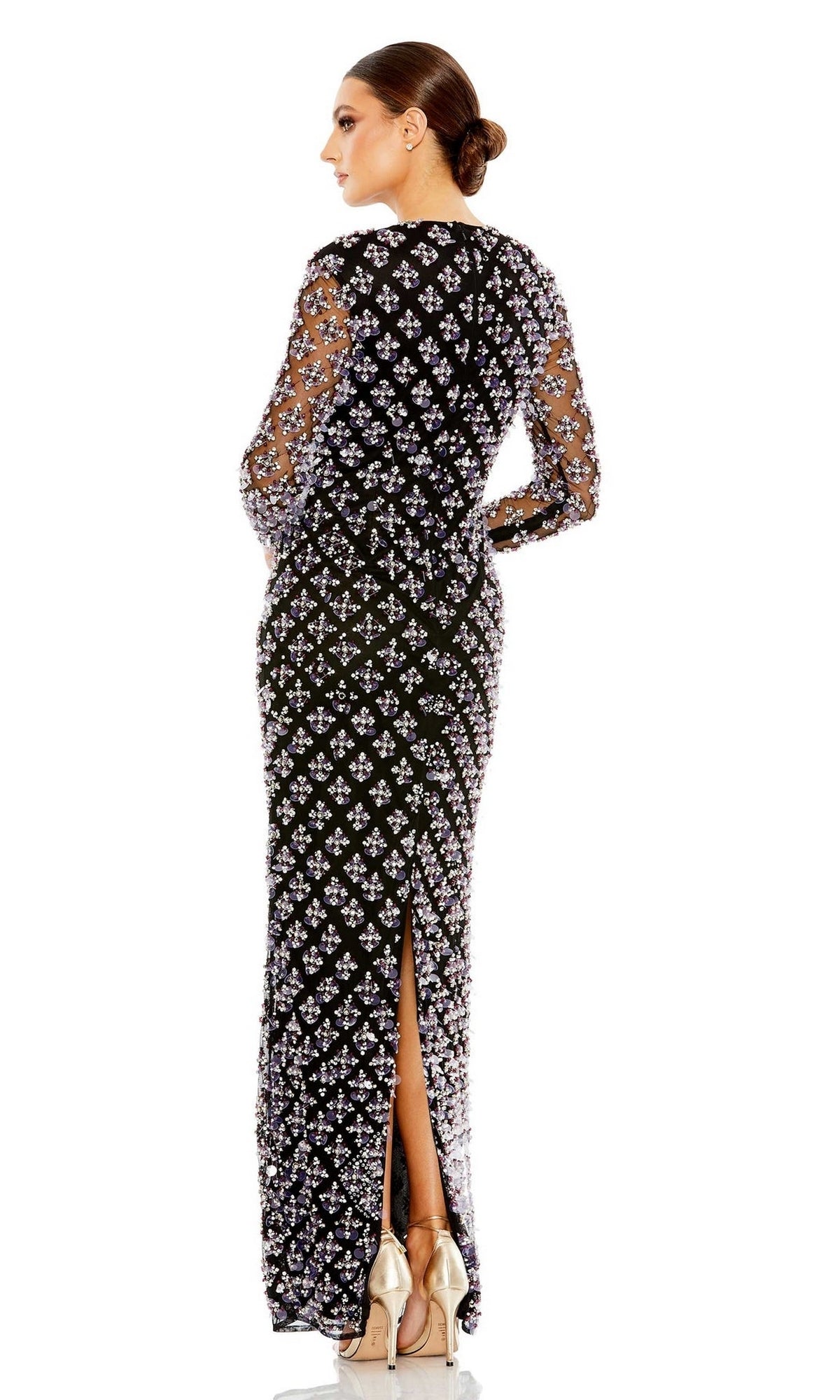 A woman in profile wears Long Formal Dress 93618 by Mac Duggal, a black floor-length gown with sheer floral long sleeves, back slit, and paired with high heels. Her hair is styled in a low bun.