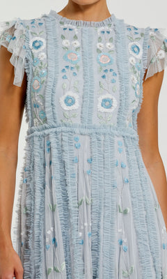 A person wearing the Mac Duggal 9366 long formal dress in light blue, featuring ruffled details and delicate floral embroidery in white, blue, green, and pink on an elegant A-line skirt.