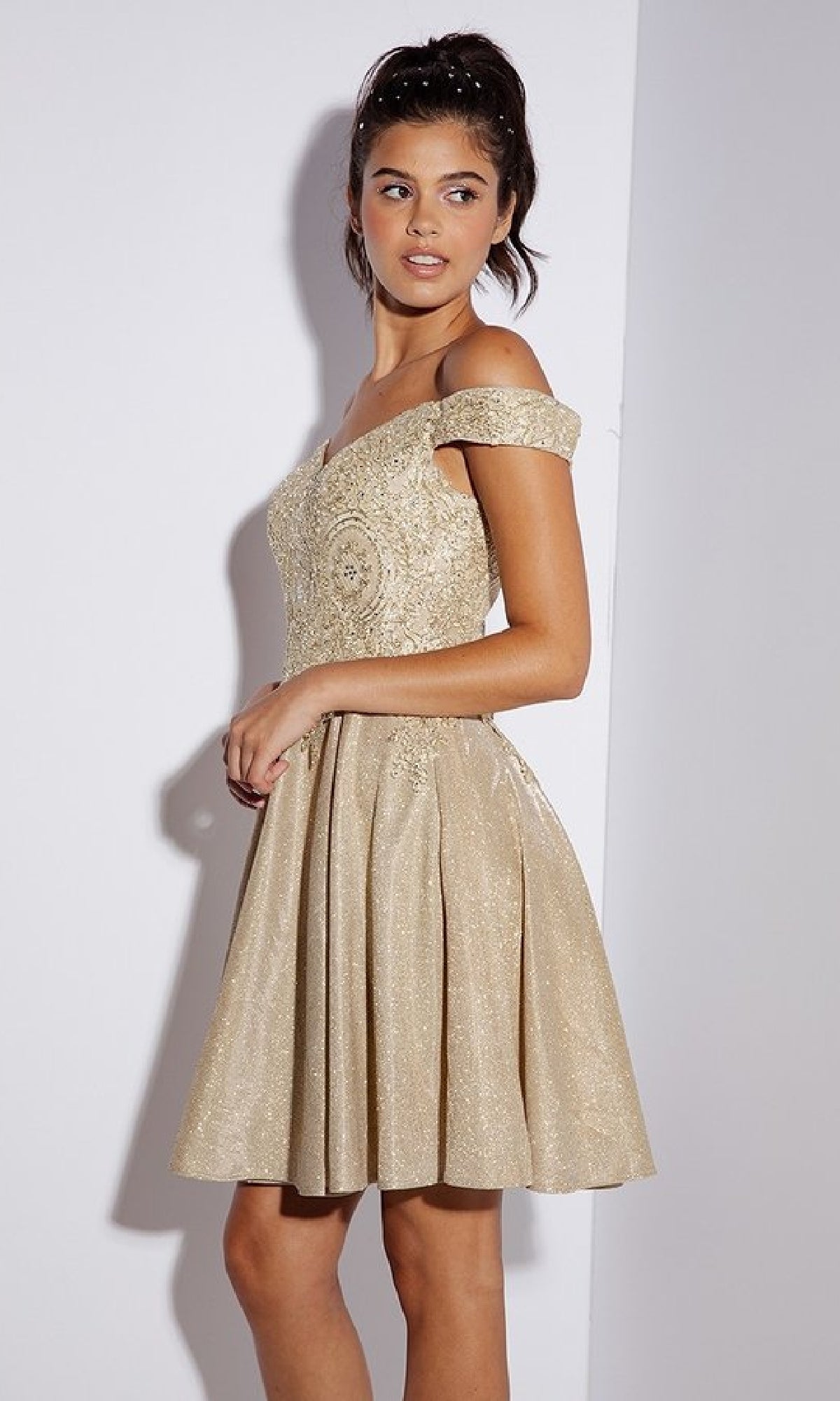 A woman poses against a plain background, wearing the Eureka 9366 Off-Shoulder Short Glitter Hoco Dress featuring a beige fitted lace bodice and a flared, knee-length skirt.