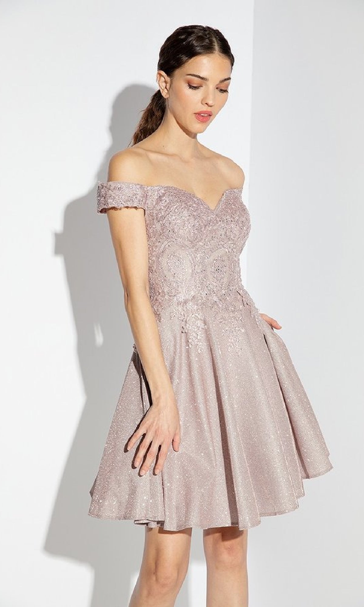 Woman wearing the Eureka 9366 Off-Shoulder Short Glitter Hoco Dress in light mauve, featuring a fitted bodice and flared skirt, standing against a plain white background.