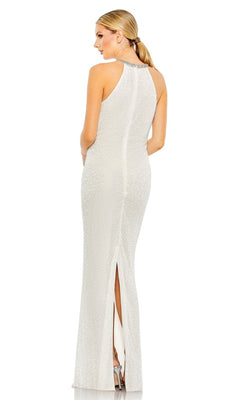 A woman stands with her back to the camera, modeling the Mac Duggal 93742—an elegant long black beaded formal dress featuring a sleeveless design, floor-length textured fabric, a side slit, and a beaded neckline.
