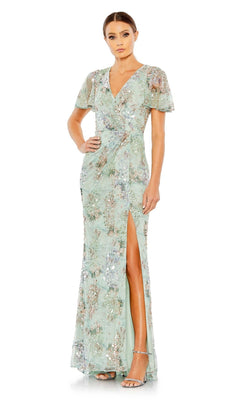 A woman poses with one hand on her hip, wearing the Mac Duggal 93749 Short Sleeve Beaded Formal Dress in light green, featuring floral patterns, a V-neckline, and a thigh-high slit.
