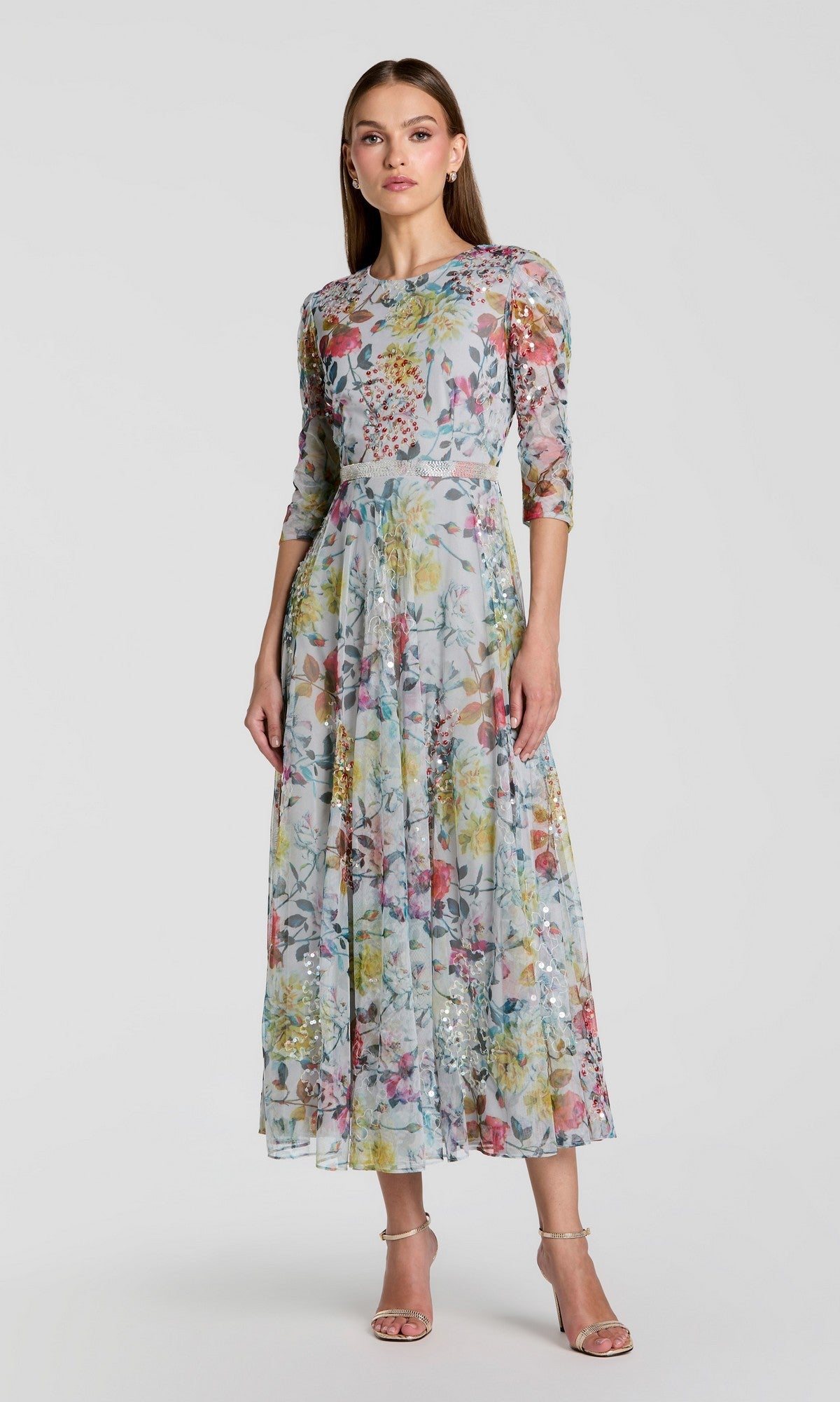 Woman standing in the Tea-Length Party Dress: Mac Duggal 93793 in a multi floral print with three-quarter sleeves and silver high-heeled sandals against a plain light background—a perfect choice for a wedding guest dress.