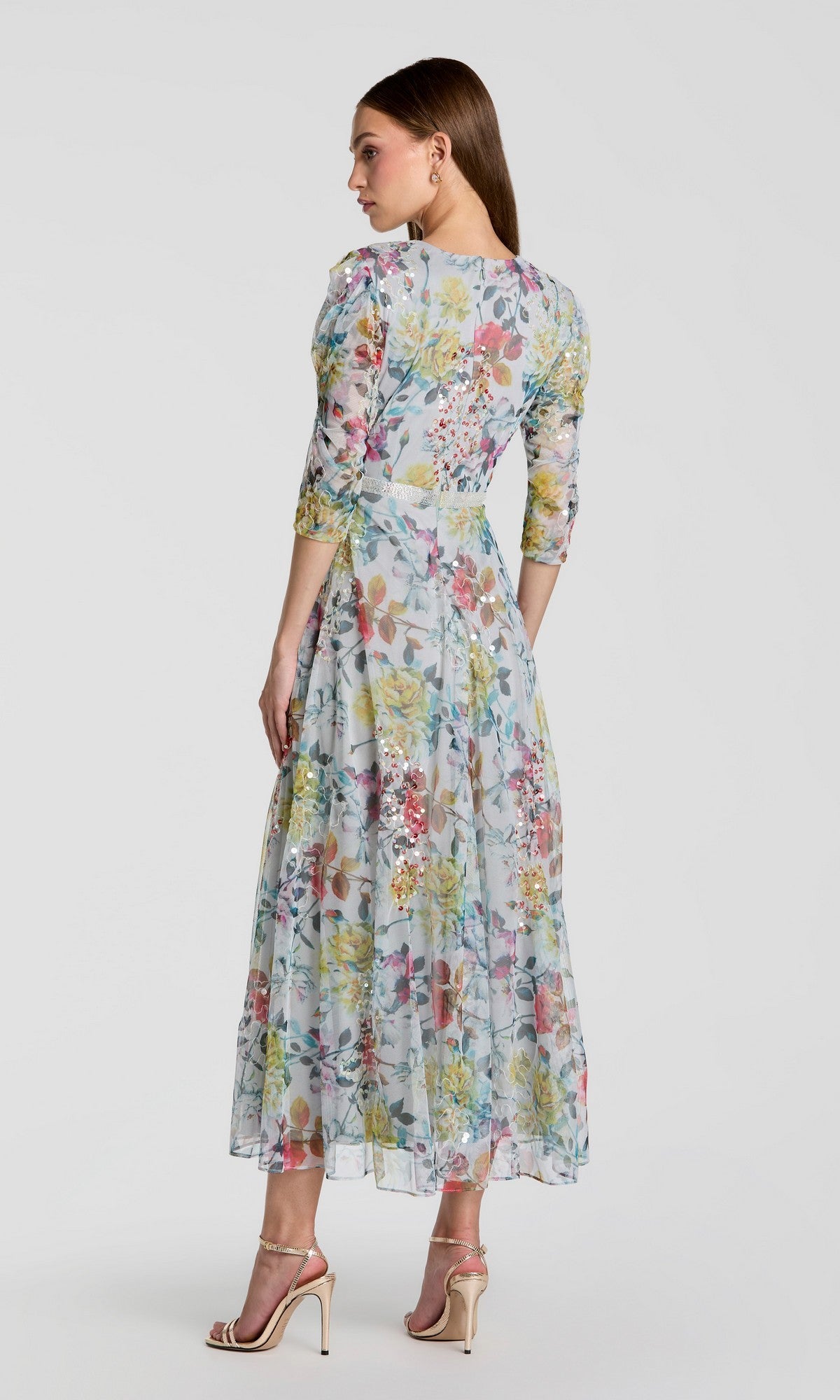 Woman standing in profile, wearing the Tea-Length Party Dress: Mac Duggal 93793, featuring three-quarter sleeves and a sheer overlay with a floral design, paired with beige high-heeled sandals—an elegant choice for a wedding guest dress.