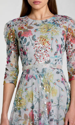 A woman wearing the Mac Duggal 93793 Tea-Length Party Dress, featuring light floral patterns, sequin embellishments, three-quarter sleeves, and a fitted waist—perfect as a chic choice for a wedding guest.
