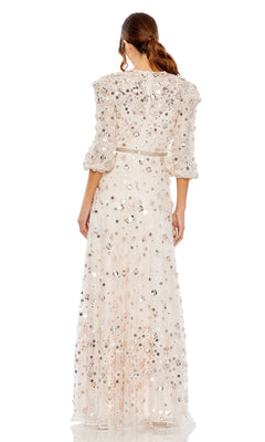 A woman stands facing away in the Mac Duggal 93805 modest long sleeve formal dress, featuring sequin and bead embellishments, sheer three-quarter sleeves, and a floor-length design in a light, elegant hue.