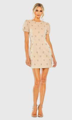A woman stands against a plain light background wearing the Mac Duggal 93836 Short Party Dress—a nude pink mini dress featuring puff sleeves and delicate floral embellishments—paired with strappy heels for an elegant, feminine look.