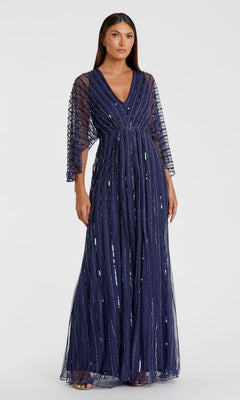 A woman stands against a plain white background, wearing the Mac Duggal 93841—a Long Sequin A-Line Formal Dress featuring navy blue sequins, sheer sleeves, and vertical stripes.