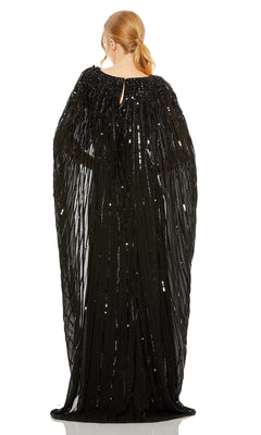 A person faces away, wearing the Mac Duggal 93869 Caped Long Sequin Formal Dress featuring a cape-style silhouette and sheer, draped fabric, with their hair in a low ponytail.