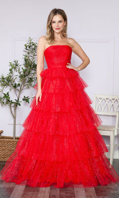 A woman in the Strapless Long Tiered Glitter Prom Ball Gown 9386—an elegant, floor-length red tulle dress with layered ruffles—stands indoors next to a white chair and a potted plant.