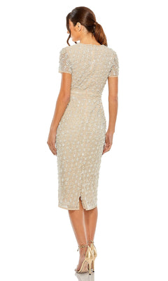 A woman with a ponytail, standing in high heels with her back to the camera, wears the Mac Duggal 93893 midi wedding-guest dress—a short-sleeved, knee-length design featuring embellished, textured details.