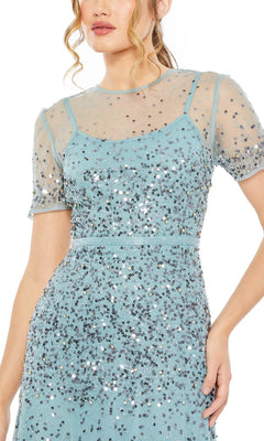 A woman wearing the Mac Duggal Sheer High-Neck Sequin Formal Dress 93909, featuring a light blue color, short sleeves, sheer overlay, and silver sequin embellishments.