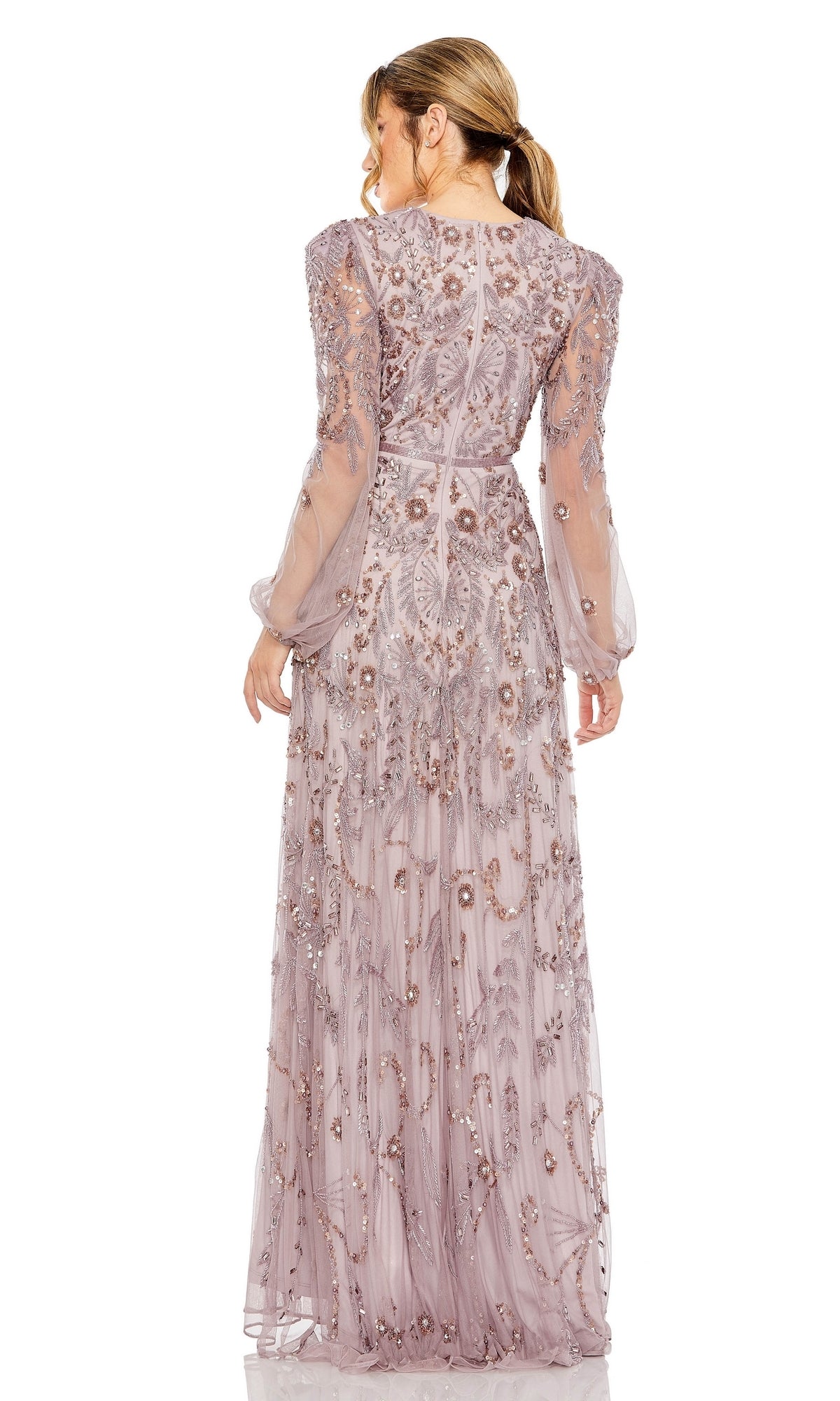 A woman with her hair in a ponytail faces away, wearing the Mac Duggal 93930 long sleeve beaded formal gown—a sheer lavender dress adorned with floral embroidery and bead embellishments.