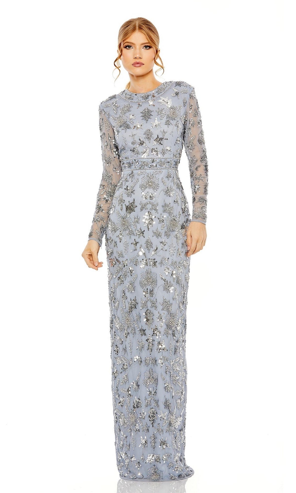 A woman wearing the Mac Duggal Slate Blue Sequin Formal Dress 93939, featuring silver floral embellishments and long sleeves, stands against a plain white background.