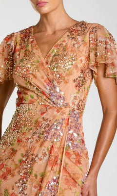 A person wearing the Mac Duggal 93949 Midi Wedding Guest Dress in peach, with flutter sleeves, floral pattern, and sparkling sequin embellishments.