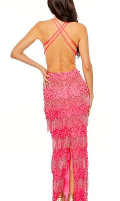 A woman stands facing away, wearing the Mac Duggal Backless Beaded Formal Dress 93956—a bright pink v-neck gown with crisscross straps, beaded fringe layers, and intricate detailing.