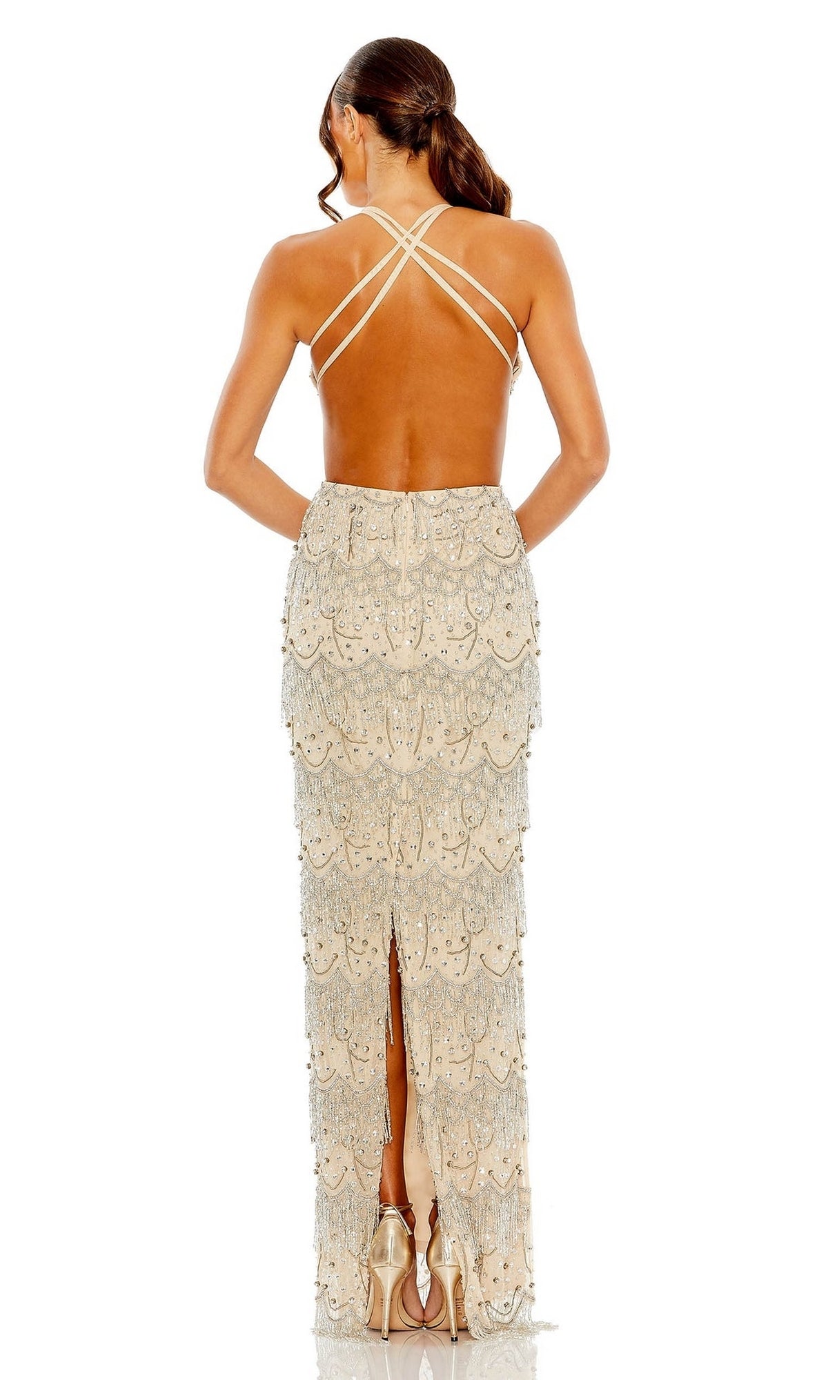 A woman faces away, wearing the Mac Duggal Backless Beaded Formal Dress 93956 with gold embellished crisscross straps and tiered beaded fringe, paired with high heels on a white background.