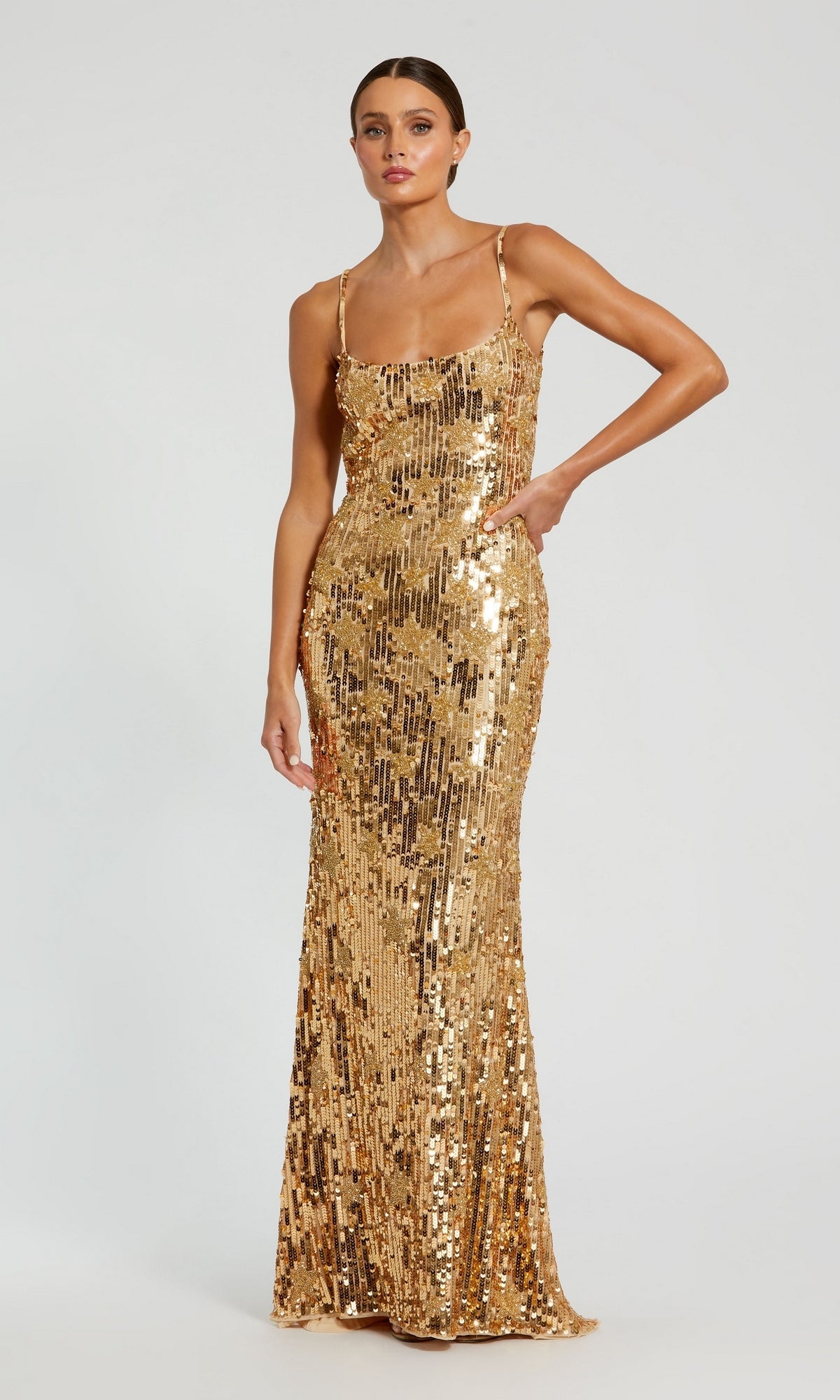 A woman stands against a plain light background wearing the Mac Duggal Long Formal Dress 93968—a sleeveless, floor-length gown with thin straps, crafted from shimmering gold sequins.