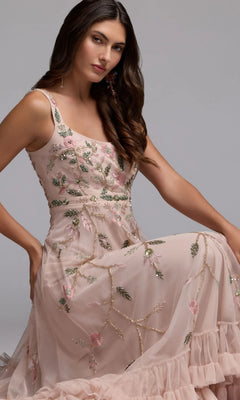 A woman wearing the Mac Duggal 9402 long formal dress, a sleeveless light pink party gown with floral beaded embroidery, is seated against a plain gray background.