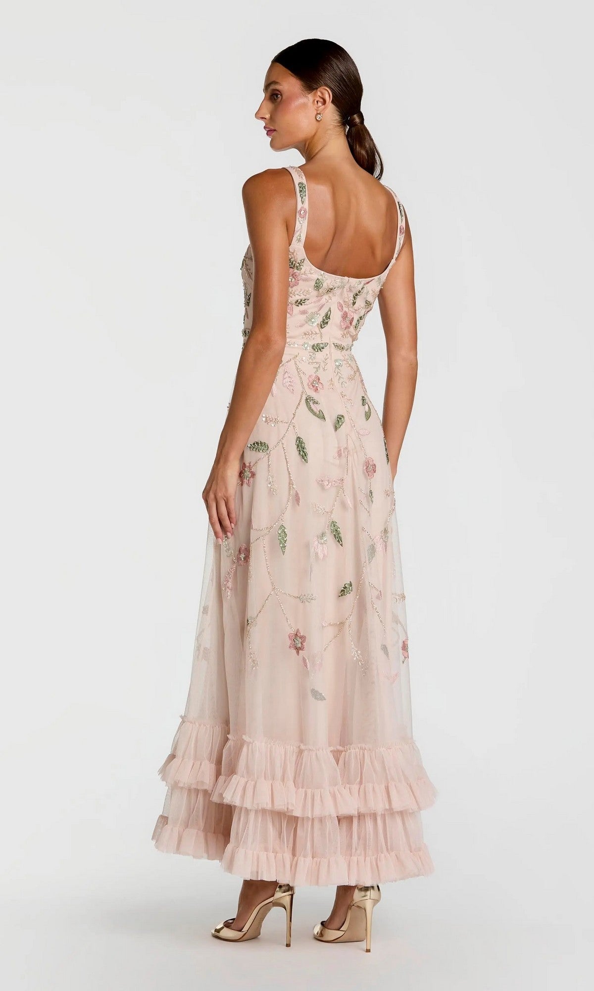 A woman stands in profile against a plain background, wearing the Long Formal Dress: Mac Duggal 9402 in light pink, which features floral beaded embroidery and a tiered ruffle hem.