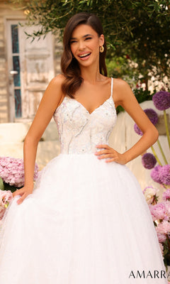 A woman in a white Amarra Sequin-Bodice Long A-Line Prom Dress 94020 stands smiling outdoors, with pink flowers and greenery behind her. The "AMARRA" logo is visible in the bottom right corner.