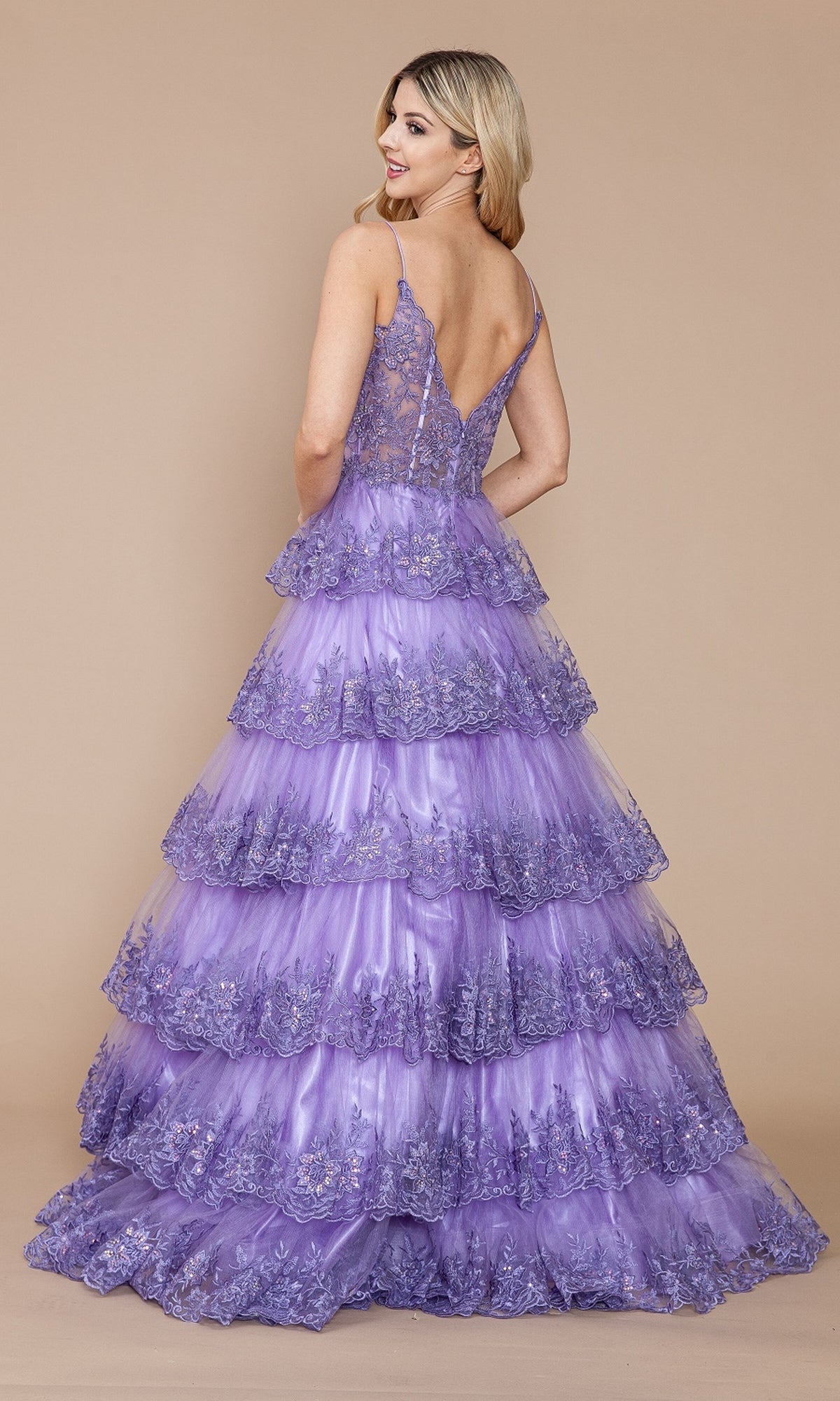 A woman in the Sheer-Bodice Long Ruffle Prom Ball Gown: Poly 9402, featuring a sleeveless embroidered-lace bodice and tiered skirt in lavender, stands slightly turned away against a plain beige background.