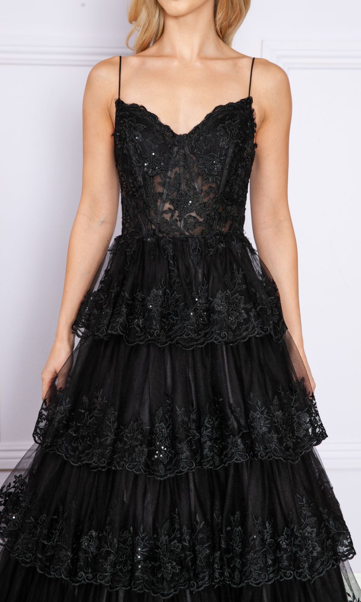 A woman stands against a light background wearing the Sheer-Bodice Long Ruffle Prom Ball Gown: Poly 9402, featuring an embroidered black sleeveless bodice with thin straps and tiered semi-sheer layers.