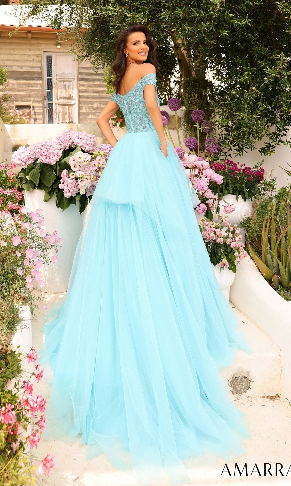 Woman in the Beaded-Bodice Long A-Line Prom Dress: Amarra 94038 stands outdoors, surrounded by pink and purple flowers and greenery, smiling over her shoulder.